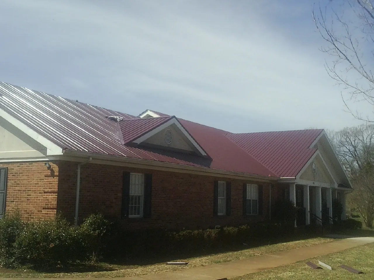 Red metal roof with gabled entries on a long brick building, from a Hail Damage Roof Repair job in Millsboro