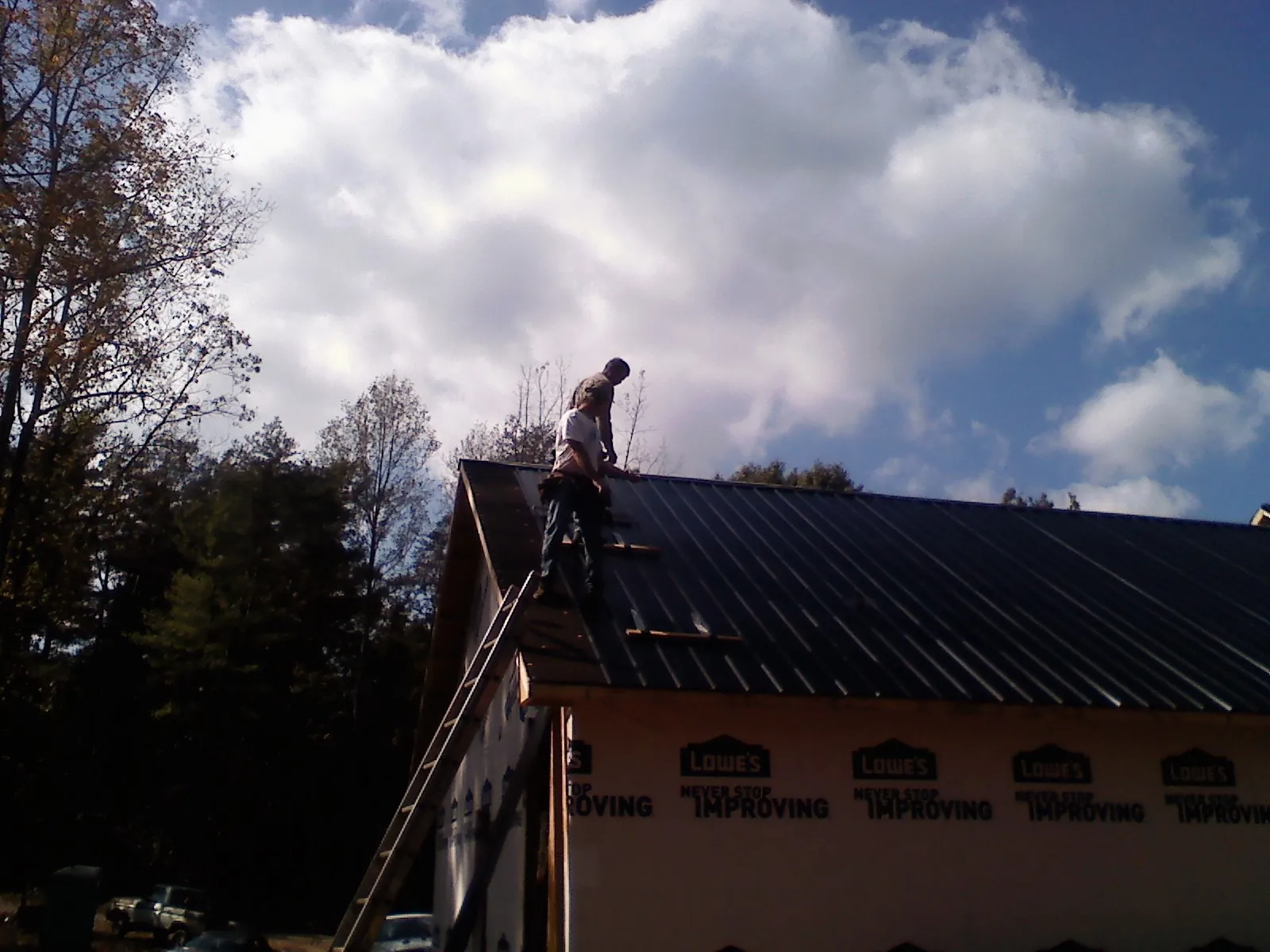 Roofer fastening dark metal panels high against a cloudy sky, from a Roof Inspection job in Millsboro