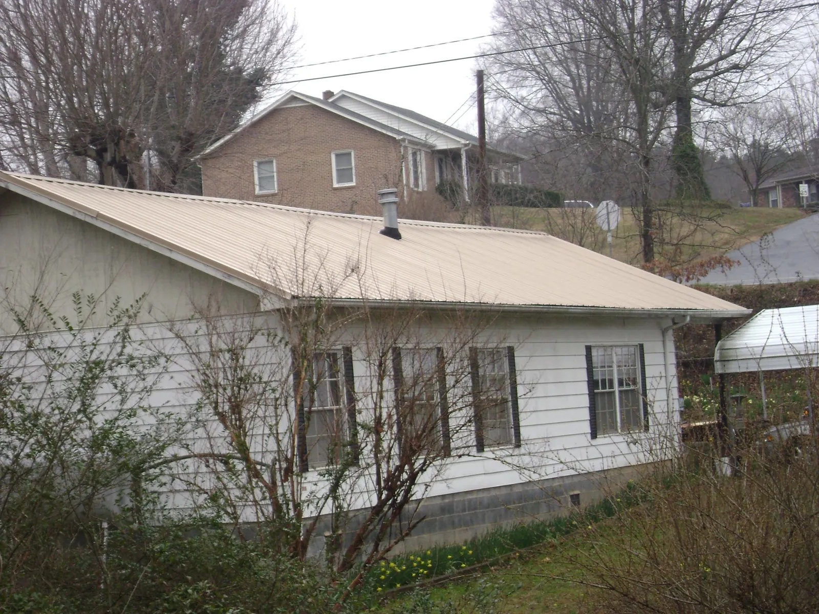 Tan metal roof on a white sided house set into a hillside — Commercial Roofing by Roofing Brothers in Millsboro